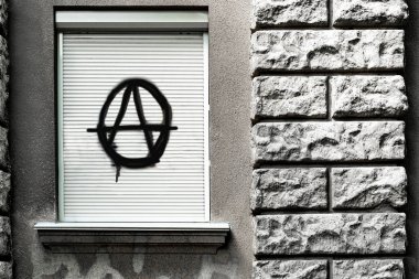 Kapalı pencerede kara bir anarşi işareti var. Anarşistler, serseriler ve sokak gösterileri kültürü. Pencereye anarşi sembolü çizilmiş