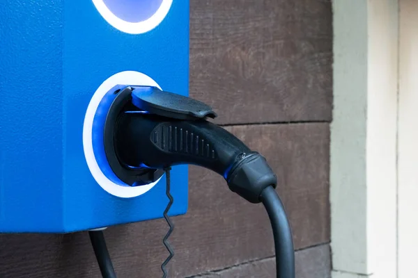 Electric car charger with blue electric car charging station on a city street. Close up of power supply plugged into a power socket