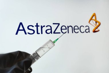 AstraZeneca Oxford COVID aşısı konsepti. Elinde şırınga tutan bir tıp çalışanı bulanık arka planda AstraZeneca logosu. Kyiv, Ukrayna - 18 Nisan 2021