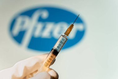 Kyiv, Ukrayna - 18 Nisan 2021: Pfizer-BioNTech aşısının sağlık hizmeti kavramı. Arka planda bulanık Pfizer şirketinin logosunun önündeki tıbbi şırınga.