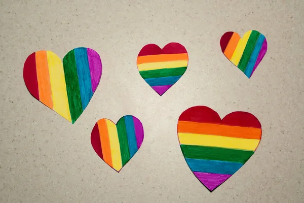 several paper LGBT-colored hearts are laid out on the gray dot background, selective focus. LGBTQ rainbow heart concept for lesbian, gay, bisexual, transgender, and queer people