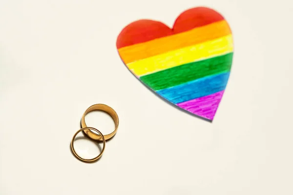 2つの黄金のリングと紙の切り絵の心Lgbtのフラグのように色 レズビアン バイセクシャル トランスジェンダー クィアの人々の結婚と組合のためのハートコンセプト — ストック写真