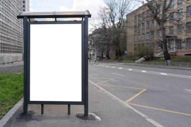 Şehir caddesindeki otobüs durağında dikey beyaz ilan panosu. Arka planda yollar ve evler var. Model yap. Caddenin yanındaki reklam panosu boş, gündüz çekimleri.