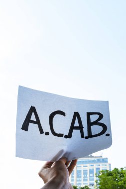 Mavi gökyüzü arka planında A.C.A.B harfleri olan bir poster tutuyor. Adalet için savaşıyor ve polis vahşetine karşı, dikey imaj