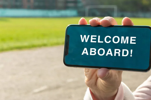Welcome aboard message on the screen of the smartphone. Woman's hand holds a smartphone and shows a message which invites a person to the team. Business concept