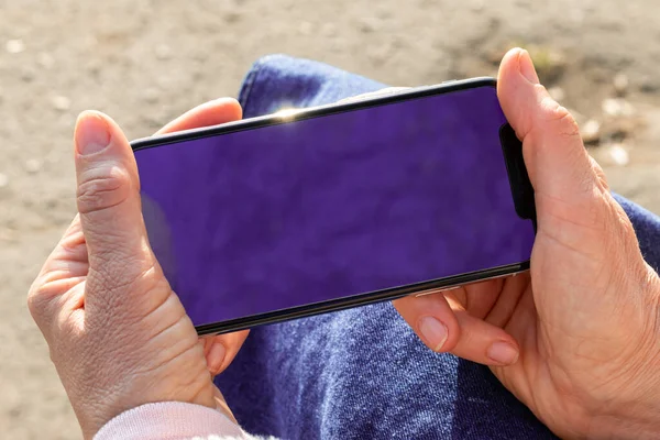 Female hands hold a new smartphone with an empty purple screen. Place for your text on the screen of a new smartphone
