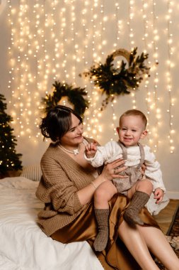 Bir anne ve çocuk bir çelenk ve Noel ağacının arkasındaki bir yatakta oturuyorlar. Çocuk çok mutlu. Yüksek kalite fotoğraf