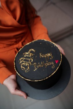 Doğum günü kızı elinde altın akreple süslenmiş siyah bir pasta tutuyor ve 