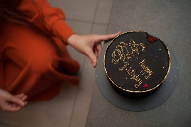 Doğum günü kızı üzerine altın harflerle süslenmiş siyah pastayı masaya yerleştirir. Mutlu yıllar. Yüksek kalite fotoğraf