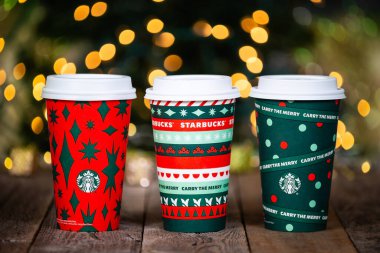 Dallas, Teksas - 12 Kasım 2020 Starbucks 'ın popüler bayram içeceği, yeni tasarlanan 2020 tatil bardaklarında servis edildi. Kırsal ahşap masada sergileniyor. Noel ağacı ışıkları arka planı bokeh.
