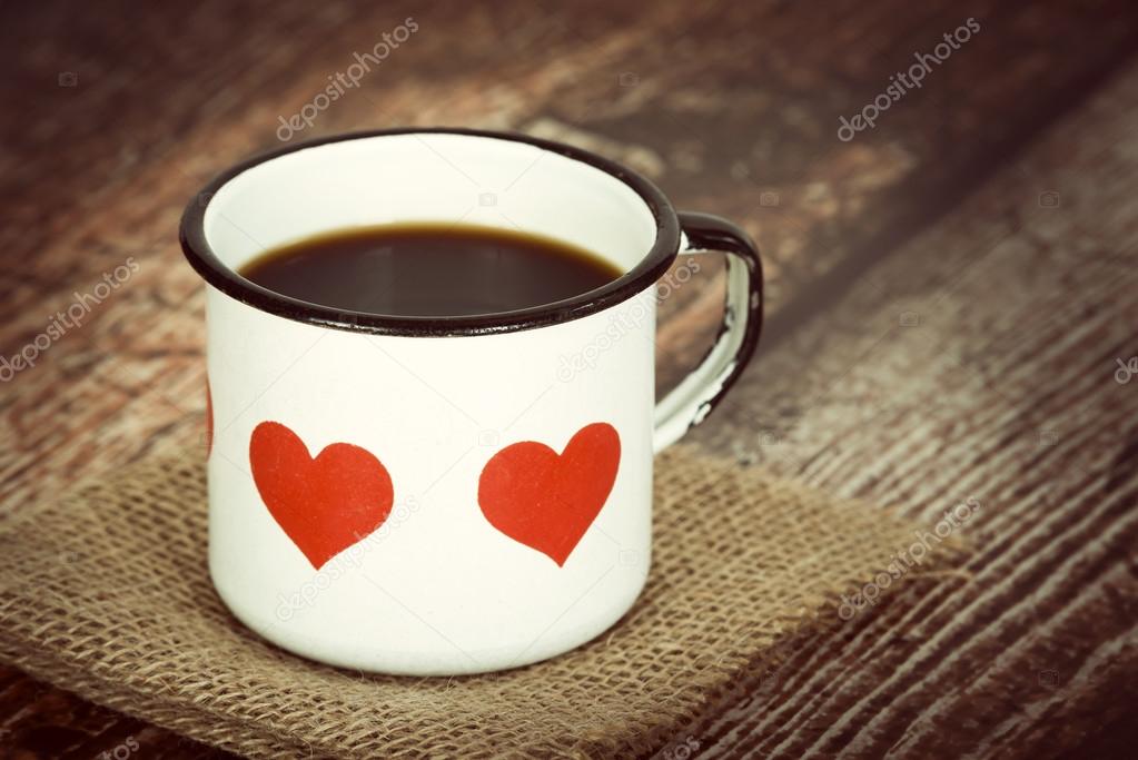 Cup of coffee in old enamel mug with hearts on rustic background