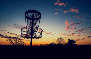 Silhouette of disc golf basket against sunset