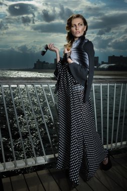 Siyah beyaz maksi elbise giyen, iskelede poz veren çekici genç kadın