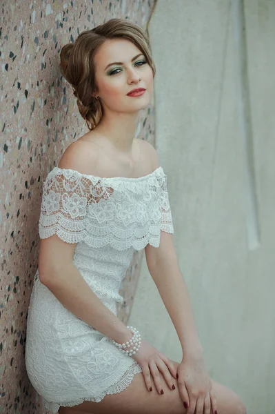 Hermosa chica elegante posando en vestido blanco corto contra fondo de pared de piedra — Foto de Stock