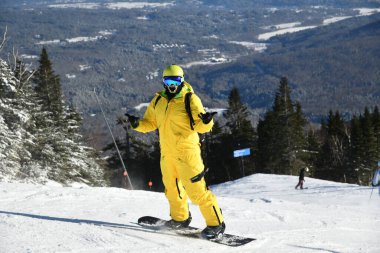 Güneşli bir günde, kar yağışlı, sarı mono takım elbiseli bir snowboardcu yamaçtan aşağı kayıyor. Stowe dağ kayak merkezi, VT 2020. Merhaba çözünürlük resmi
