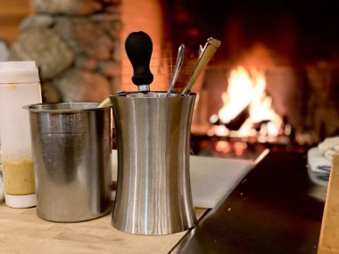 Geleneksel şöminenin önünde yemek takımı ve modern restoran içinde yanan odun ve dekorasyonlar. Şöminenin güzel manzarası sıcak ve samimi bir tablo oluşturur.. 