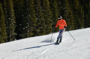 Kadın kayakçı, güneşli bir günde yüksek hızda yamaçlardan aşağı iniyor. Colorado, Vail Kayak Tesisi 'nde yeni bir gösteriyle.