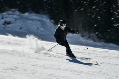 Kadın kayakçı, güneşli bir günde yüksek hızda yamaçlardan aşağı iniyor. Colorado, Vail Kayak Tesisi 'nde yeni bir gösteriyle.