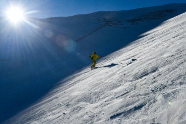Sarı takım elbiseli bir adam kar tepesinde snowboard yapıyor. Aşırı kış sporları. Aksiyon atışı. Breckenridge, komutan.