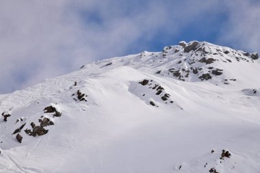 Derin mavi gökyüzünün altındaki karla kaplı dağ zirvesi. Rocky yamaçları ve taze kış karı dramatik bir alp manzarası yaratır. Doğa, macera ve kış yolculuğu temaları için mükemmeldir..