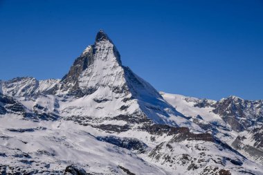 İsviçre Alpleri 'ndeki ikonik Matterhorn zirvesinin göz kamaştırıcı kış manzarası. Parlak mavi gökyüzü, dramatik karlı yamaçlar ve detaylı dağ dokuları seyahat ve doğa temaları için mükemmel görkemli bir dağ manzarası yaratır..