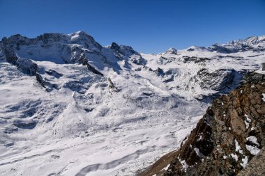 İsviçre Alpleri 'ndeki ikonik Matterhorn zirvesinin göz kamaştırıcı kış manzarası. Parlak mavi gökyüzü, dramatik karlı yamaçlar ve detaylı dağ dokuları seyahat ve doğa temaları için mükemmel görkemli bir dağ manzarası yaratır..