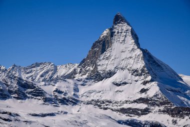 İsviçre Alpleri 'ndeki ikonik Matterhorn zirvesinin göz kamaştırıcı kış manzarası. Parlak mavi gökyüzü, dramatik karlı yamaçlar ve detaylı dağ dokuları seyahat ve doğa temaları için mükemmel görkemli bir dağ manzarası yaratır..