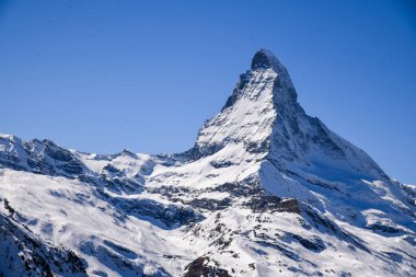 A stunning winter view of the iconic Matterhorn peak in the Swiss Alps. Clear blue sky, dramatic snowy slopes, and crisp mountain details create a majestic alpine landscape ideal for travel and nature themes.