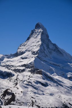 İsviçre 'nin Zermatt kentindeki kar kaplı Matterhorn zirvesinin çarpıcı dikey görüntüsü. Açık mavi gökyüzü, kışın serin manzarası ve dramatik alp manzarası seyahat, doğa ve kış sporları için mükemmel nefes kesici bir dağ manzarası yaratır..