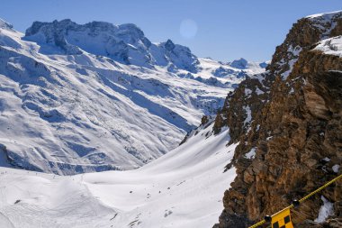 İsviçre Alpleri 'ndeki dramatik karlı dağ zirveleri parlak mavi bir gökyüzünün altında. Engebeli kayalıklar, derin gölgeler ve el değmemiş kış manzarası çarpıcı bir yüksek irtifa manzarası yaratır..