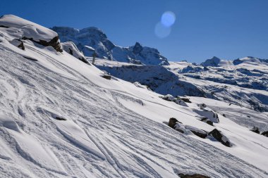 İsviçre 'nin Zermatt kentindeki karlı dağlık yamaçlarda el değmemiş toz, engebeli dağ zirveleri ve açık mavi gökyüzü. Manzaralı kış manzarası kayak, seyahat ve doğa geçmişi için mükemmel..