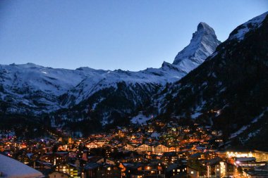 Karlı Matterhorn 'un altında parıldayan sıcak köy ışıklarıyla Zermatt' ın manzarası. Kış manzarası, dağlık dağları ve İsviçre Alpleri 'ndeki huzurlu alacakaranlık atmosferi..