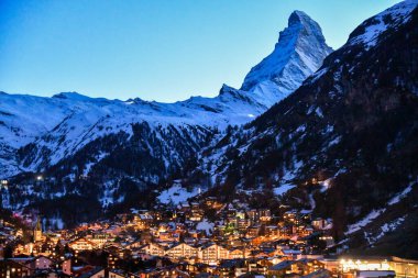 Karlı Matterhorn 'un altında parıldayan sıcak köy ışıklarıyla Zermatt' ın manzarası. Kış manzarası, dağlık dağları ve İsviçre Alpleri 'ndeki huzurlu alacakaranlık atmosferi..