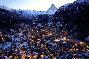 Zermatt 'ın mavi saatte parlayan hayret verici hava aracı görüntüsü, karlı dağların tepelerinde yükselen ikonik Matterhorn' lar ve aşağıdaki köyün kış ışıkları.