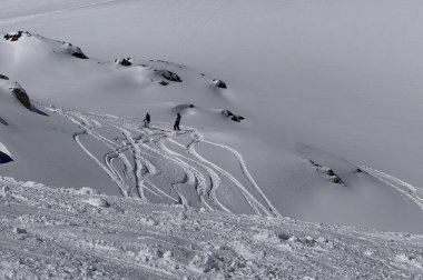 İki kayakçı, parlak kış ışığı altında karlı bir yamaçta taze izler bırakıyorlar. Dokunulmamış toz, dağ arazisi ve yokuş aşağı hareketli serbest kayak sahnesi.