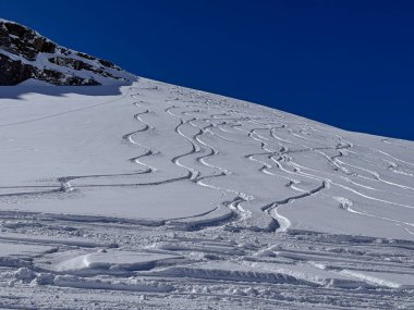 İsviçre Alplerinde el değmemiş kar yamacında taze oyulmuş kayak izleri, kış dağlarının ve el değmemiş arazinin güzelliğini yakalıyor..