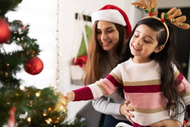 İspanyol bir annenin küçük kızına Noel ağacına bazı süsler takmasına ve iyi vakit geçirmesine yardım etmesi.