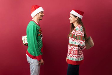 Kırmızı arka planı olan bir stüdyoda Noel hediyelerini saklayan İspanyol bir çiftin profil görüntüsü.