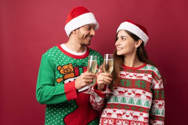 Noel Baba şapkası takan, şampanya bardakları tokuşturan ve Noel 'de kadeh kaldıran romantik bir çift.