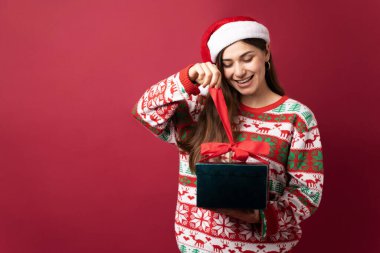 Noel Baba şapkalı esmer kadın Noel hediyesini açıyor ve heyecanlı görünüyor.