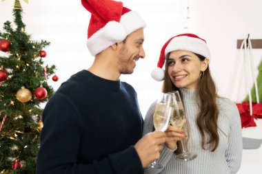 Noel Baba şapkası takan ve Noel 'de şampanya içen mutlu ve romantik bir çiftin yakın çekimi.