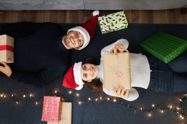 İspanyol bir çiftin evde rahatlarken ve yerde yatarken Noel hediyelerini paylaşırken yüksek açılı görüntüsü.