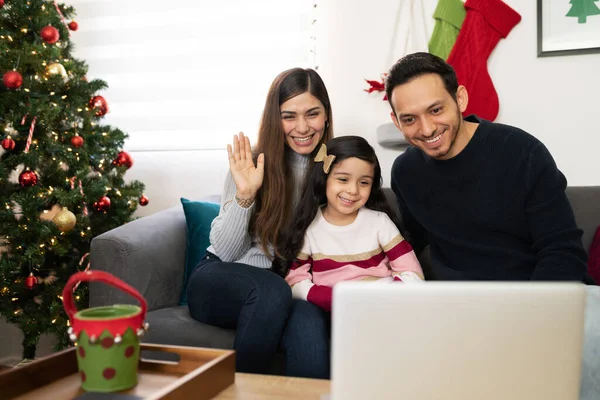 Happy Hispanic family of three saying hello to some of their relatives and parents while doing a video call on a laptop computer on Christmas