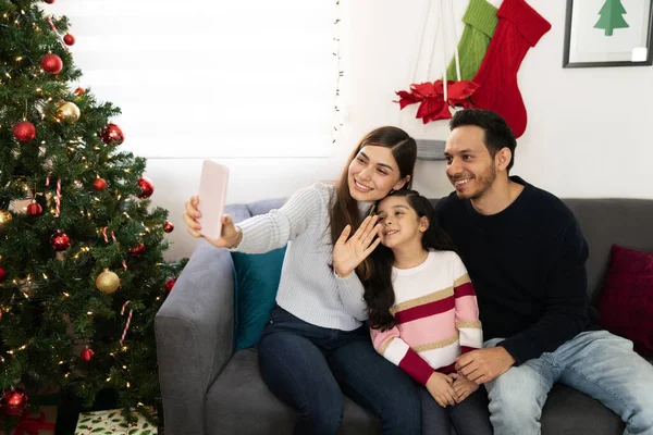 クリスマスに彼らの親戚の何人かとビデオ通話を行うためにスマートフォンを使用して3人の良い家族を見て — ストック写真