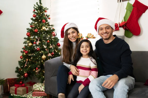 Hispanic family of three wearing Christmas hats and enjoying their time together at home on the holidays