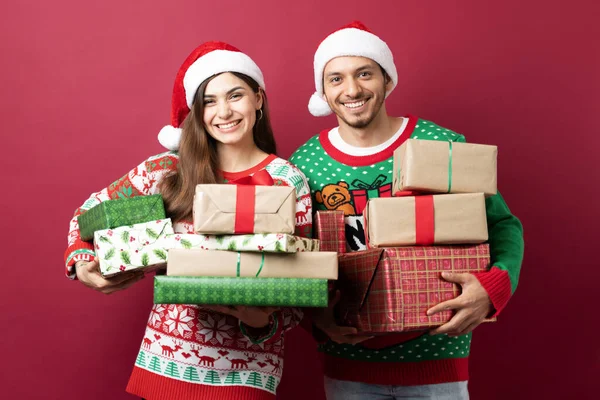 Cute Latin Couple Carrying Bunch Christmas Presents Smiling Red Background — Stock Photo, Image