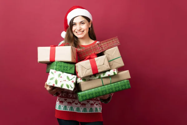 Cheerful Young Woman Wearing Santa Hat Carrying Pile Christmas Presents — Stock Photo, Image