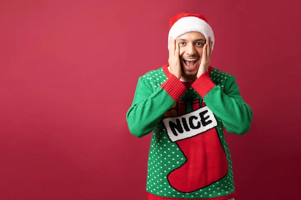 Hispanic man with ugly sweater opening his mouth and looking surprised about some awesome Christmas sale