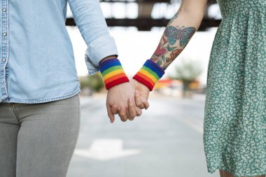 Lezbiyen bir çiftin el ele tutuşması ve LGBT haklarını desteklemek için gökkuşağı eşcinsellik bilekliği takması.