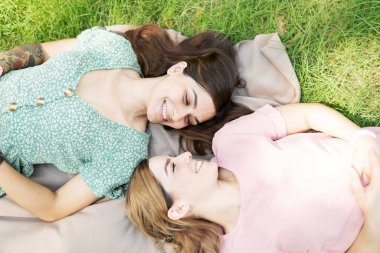 Çekici bir lezbiyen çiftin, çimenlerde bir battaniyenin üzerinde yatarken romantik bir şekilde gözlerinin içine bakması.